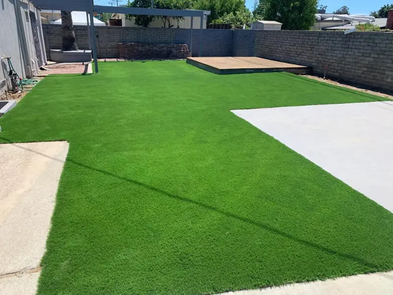 Artificial turf lawn laid alongside a concrete walkway and retaining wall